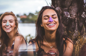 Two girls outside smiling while wearing Nöz spf for face on their nose. Product shown in colors blue and purple.